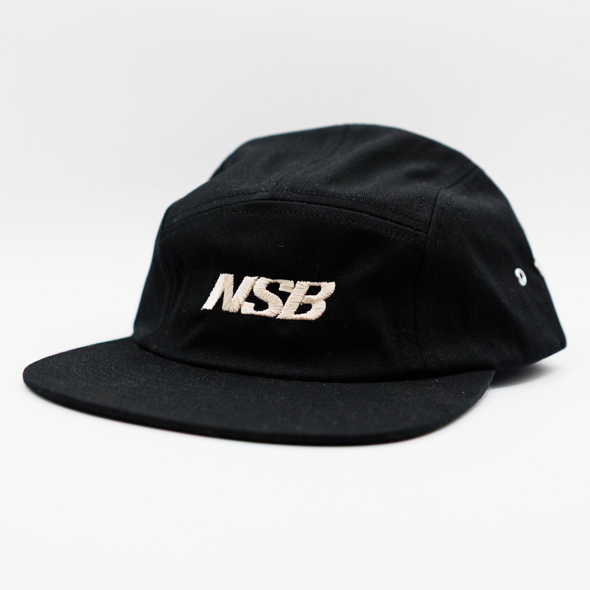 A black five-panel camp cap with a flat brim, featuring the letters 'NSB' embroidered in a metallic white tone on the front, set against a plain white background.